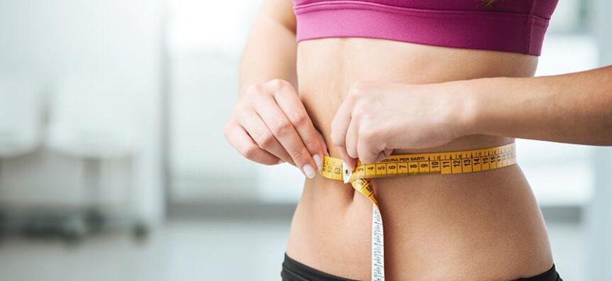 The girl measures her waist size.